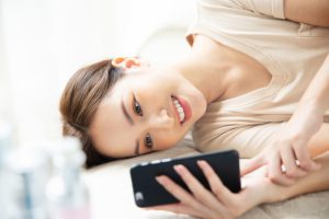 ベッドで横たわってスマホをいじる女性