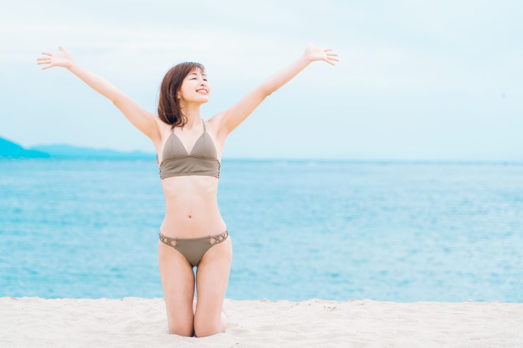 砂浜で膝立ちする水着の女性